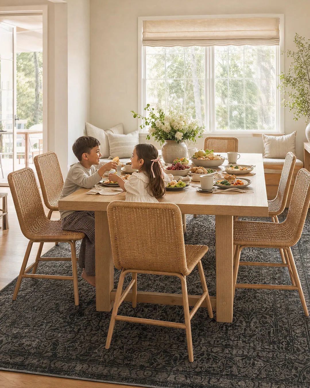 Two children sitting at a dining table in a bright, well-lit room with large windows.