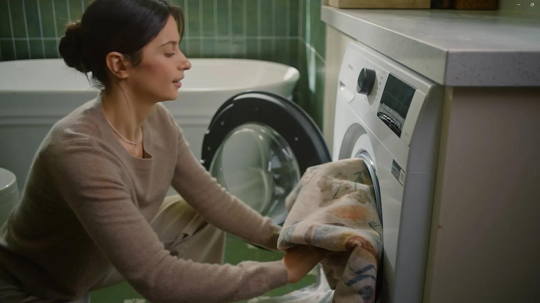 Woman loads patterned bedding into modern white washing machine