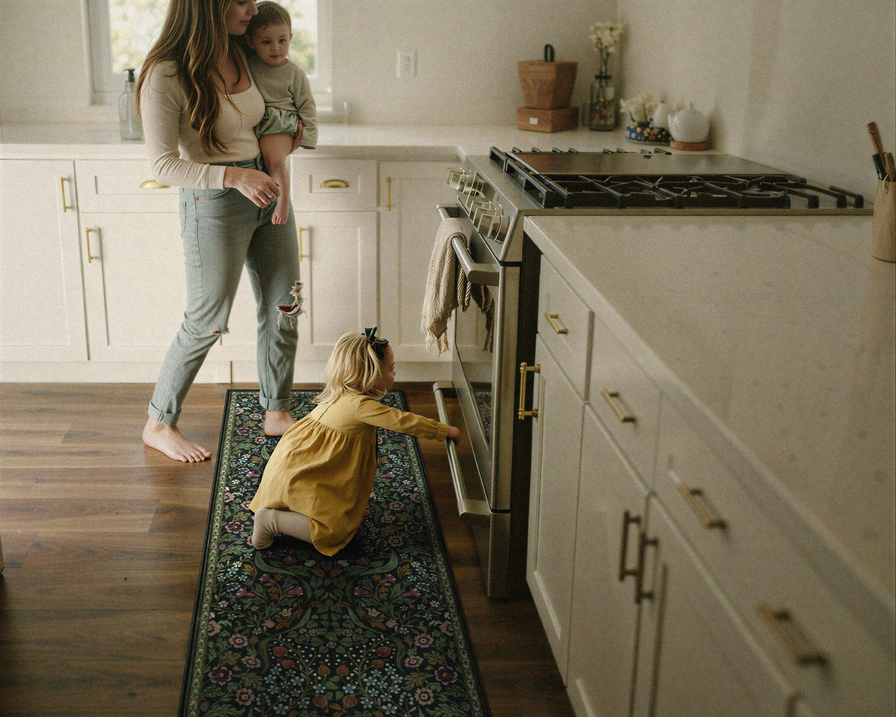Woman holding a child and another child reaching into an open oven in a kitchen.