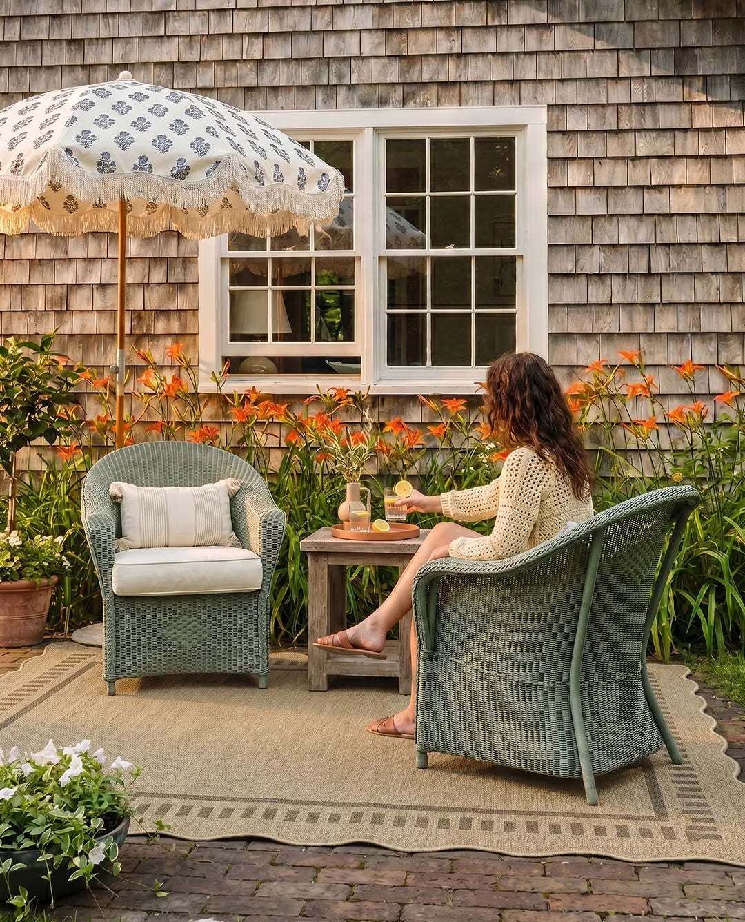Woman sitting in a wicker chair under an umbrella in a garden setting.